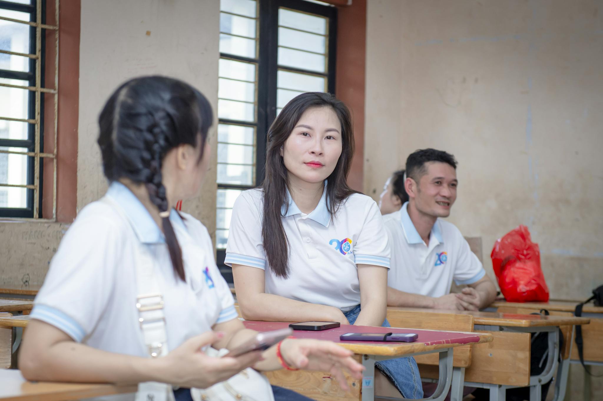Three adults having a casual discussion in a classroom setting in Hanoi, Vietnam.